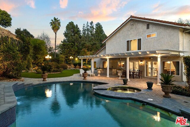 pool at dusk featuring an in ground hot tub, a patio area, and a pergola