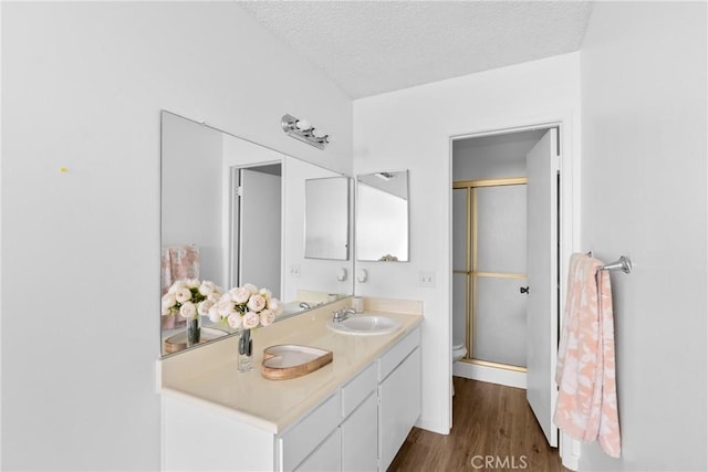 bathroom featuring hardwood / wood-style flooring, vanity, walk in shower, toilet, and a textured ceiling