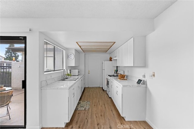 kitchen with sink, white appliances, a textured ceiling, white cabinets, and light wood-type flooring