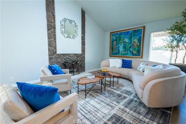 living room featuring lofted ceiling, a stone fireplace, and wood-type flooring