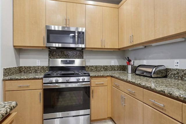 kitchen with stainless steel appliances, dark stone counters, and light brown cabinets