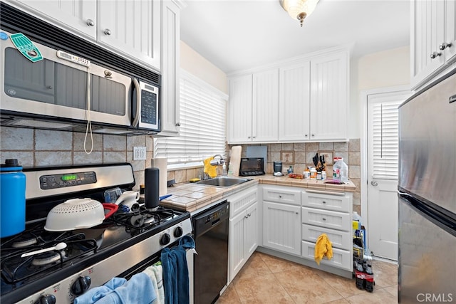 kitchen with sink, tile counters, white cabinets, stainless steel appliances, and backsplash