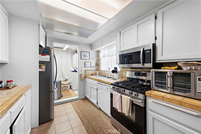 kitchen with white cabinetry, appliances with stainless steel finishes, tile countertops, and light tile patterned flooring