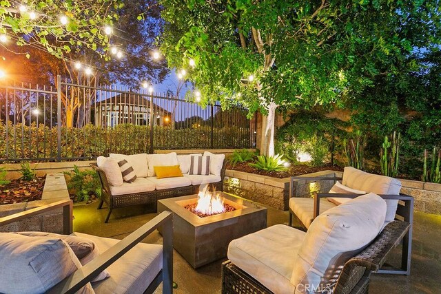 patio at night with fence and an outdoor living space with a fire pit