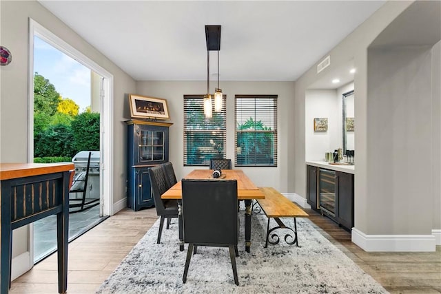 dining space featuring a healthy amount of sunlight, beverage cooler, and light wood-type flooring