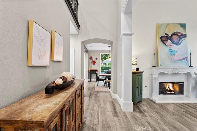 hall with arched walkways, baseboards, a high ceiling, and light wood finished floors