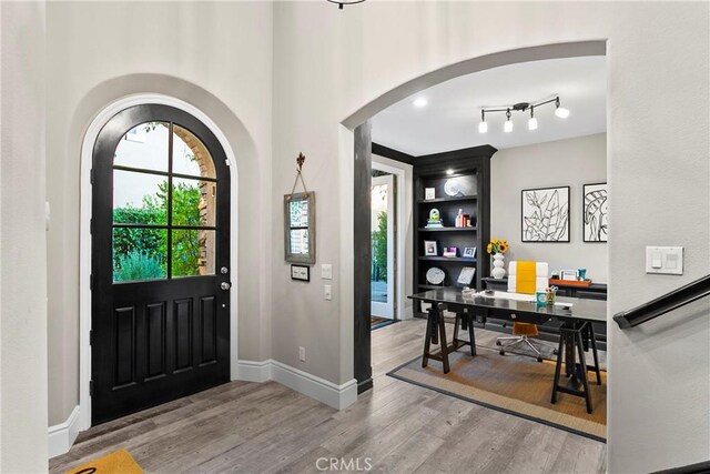 foyer entrance featuring baseboards, arched walkways, and wood finished floors