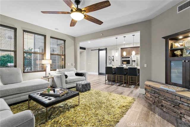 living room with light hardwood / wood-style flooring, a barn door, and ceiling fan