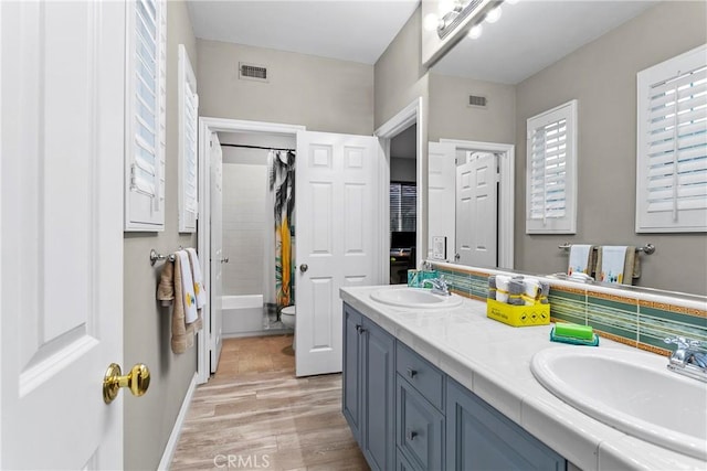 full bathroom with hardwood / wood-style flooring, shower / bath combo, vanity, decorative backsplash, and toilet