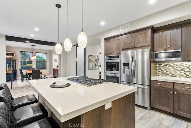 kitchen featuring backsplash, hanging light fixtures, a center island, stainless steel appliances, and dark brown cabinets