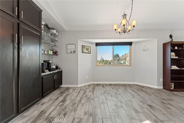 unfurnished dining area featuring a notable chandelier, light wood-type flooring, and baseboards