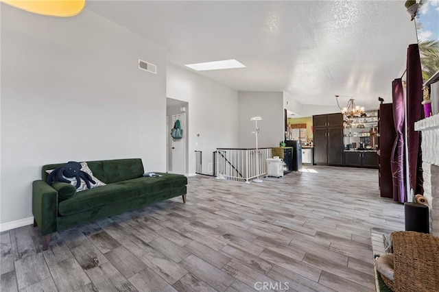 living area featuring a chandelier, vaulted ceiling with skylight, light wood-style flooring, and visible vents