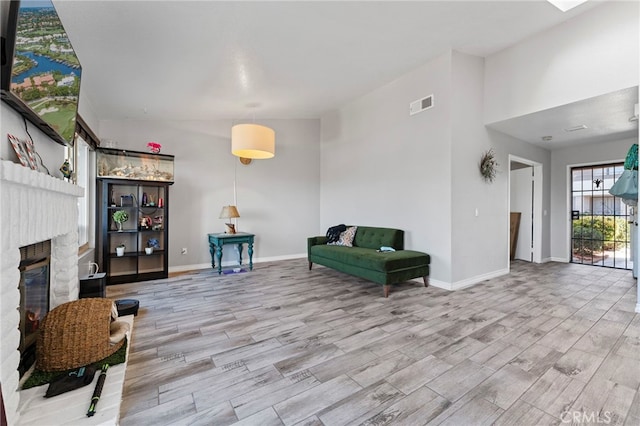 interior space with a brick fireplace, visible vents, baseboards, and wood finished floors