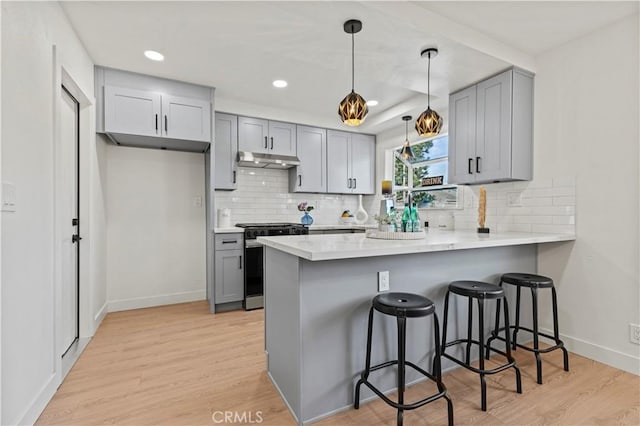 kitchen with gas range, gray cabinets, kitchen peninsula, and a breakfast bar