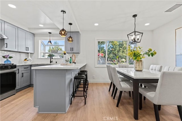 kitchen with gray cabinetry, decorative light fixtures, a kitchen breakfast bar, stove, and backsplash