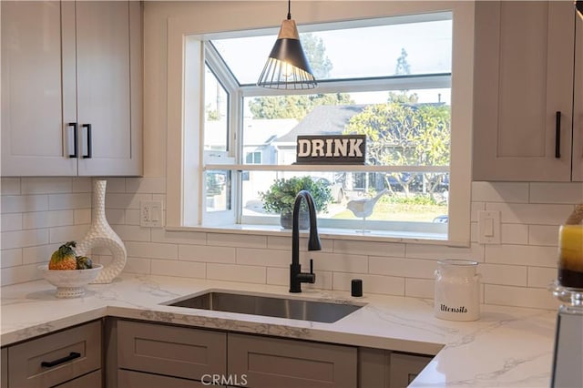 kitchen with sink, gray cabinetry, hanging light fixtures, a healthy amount of sunlight, and light stone countertops