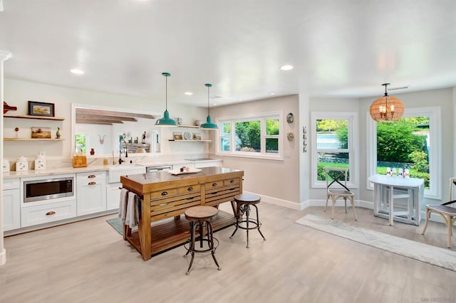 kitchen featuring stainless steel microwave, decorative light fixtures, white cabinets, and light wood-type flooring