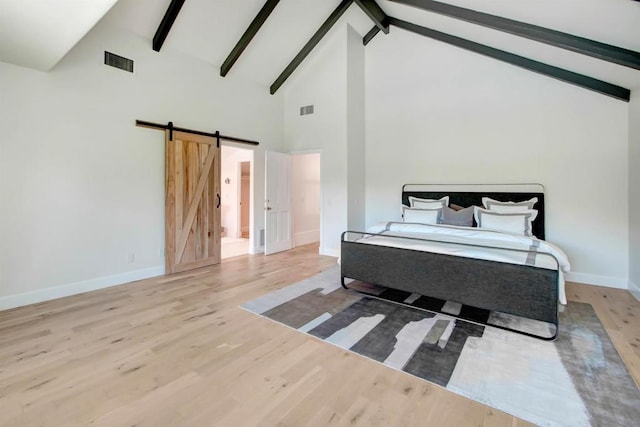 bedroom with beamed ceiling, a barn door, high vaulted ceiling, and light wood-type flooring