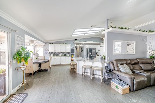 living room featuring sink, vaulted ceiling, ornamental molding, and light wood-type flooring