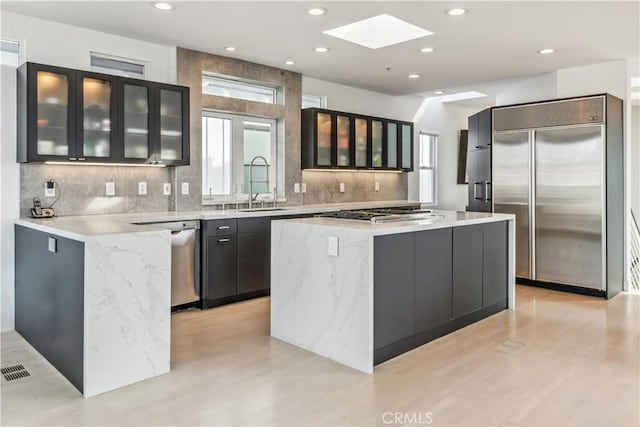 kitchen with a skylight, sink, a center island, stainless steel appliances, and light stone countertops