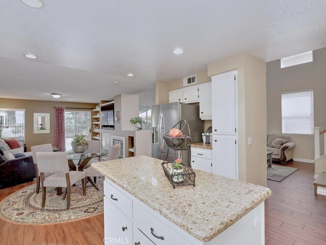 kitchen with white cabinetry, stainless steel fridge, a center island, and light hardwood / wood-style flooring