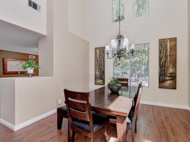 dining area with a towering ceiling, hardwood / wood-style floors, and a notable chandelier