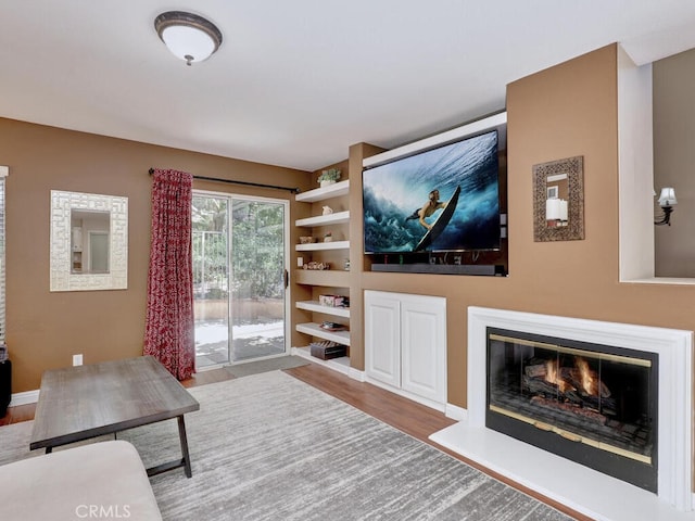 living room featuring a glass covered fireplace, baseboards, and wood finished floors