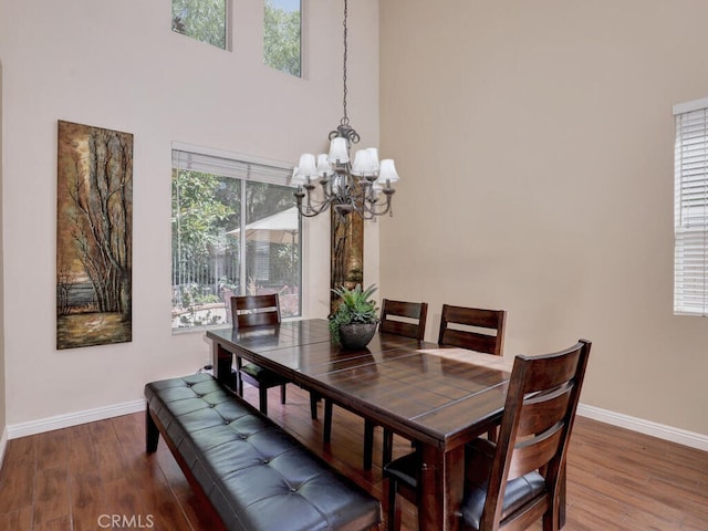 dining room featuring wood finished floors, a towering ceiling, and baseboards