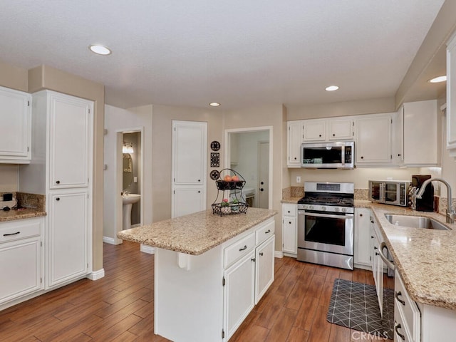 kitchen featuring stainless steel appliances, white cabinets, a sink, and wood finished floors