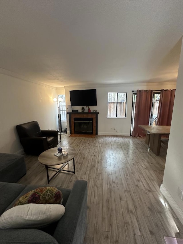 living room with crown molding, a healthy amount of sunlight, a tiled fireplace, and light wood-type flooring