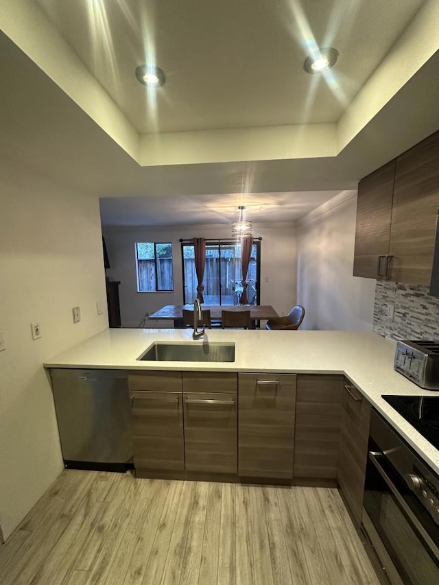 kitchen featuring kitchen peninsula, black appliances, sink, a tray ceiling, and light hardwood / wood-style flooring