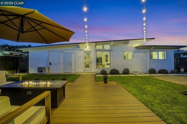 back house at dusk with a yard, a deck, and a fire pit