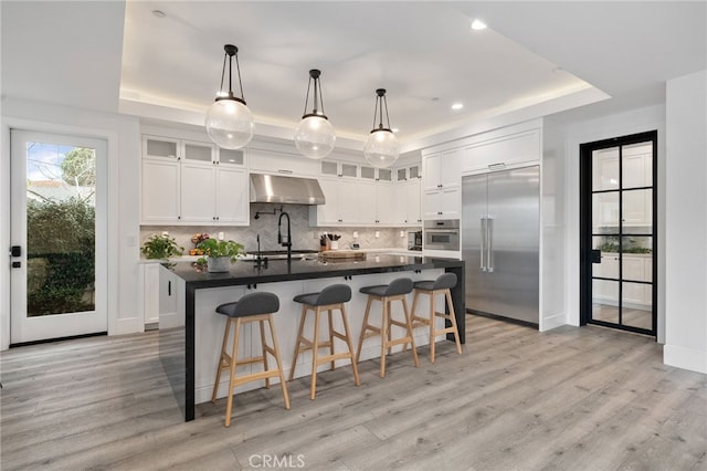 kitchen featuring a center island with sink, a tray ceiling, pendant lighting, stainless steel appliances, and white cabinets