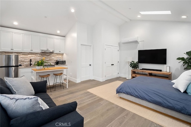 bedroom with an AC wall unit, a skylight, sink, stainless steel fridge, and light hardwood / wood-style flooring