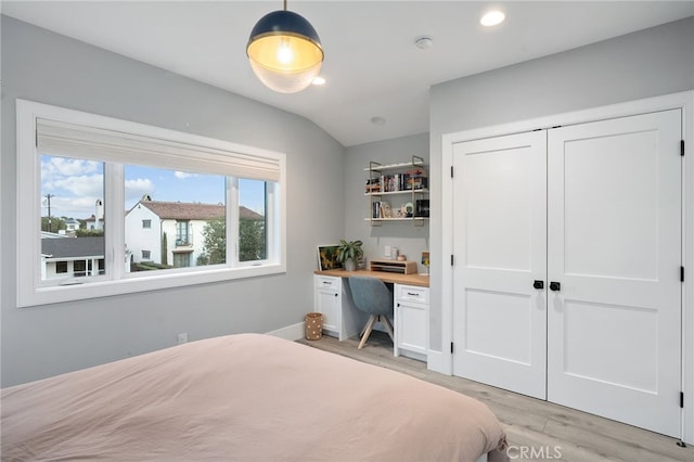 bedroom featuring vaulted ceiling, built in desk, light wood-type flooring, and a closet