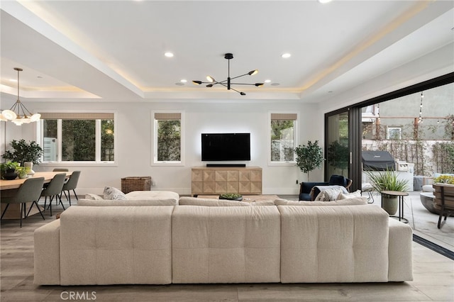 living room featuring a raised ceiling, a wealth of natural light, a notable chandelier, and light wood-type flooring