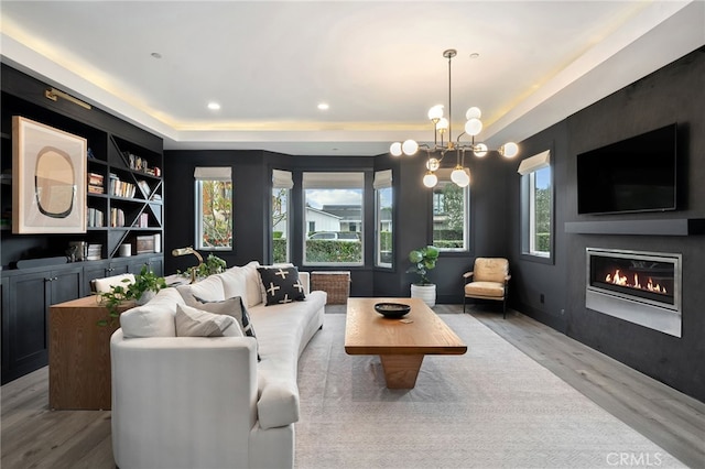 living room with hardwood / wood-style flooring, a raised ceiling, built in features, and a notable chandelier