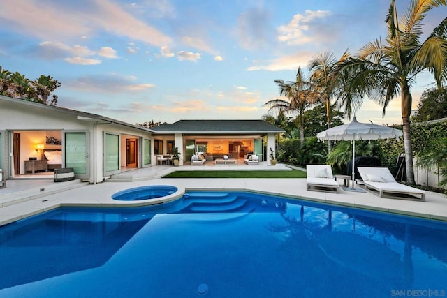 pool at dusk with an in ground hot tub, outdoor lounge area, and a patio area