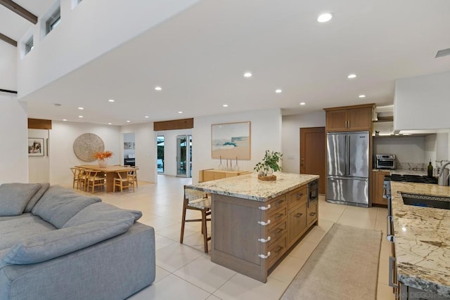 kitchen with a spacious island, a breakfast bar area, light tile patterned floors, stainless steel refrigerator, and light stone countertops