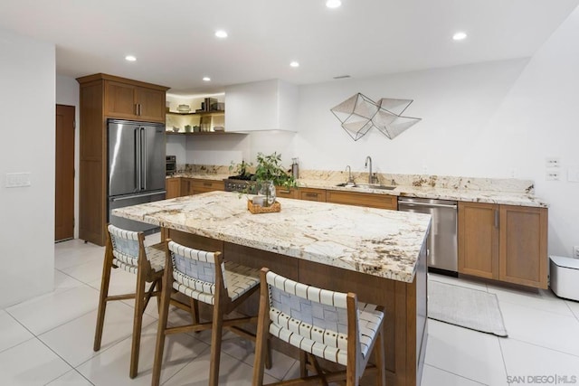 kitchen featuring sink, a breakfast bar, stainless steel appliances, light stone counters, and light tile patterned flooring