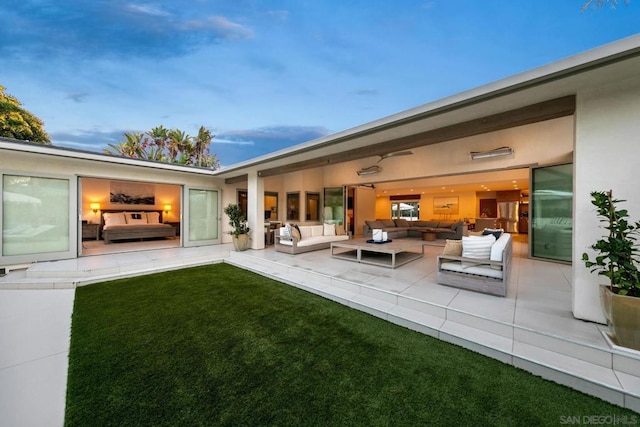 back house at dusk with an outdoor living space, a patio area, and a lawn