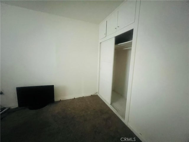 unfurnished bedroom with dark carpet and a closet