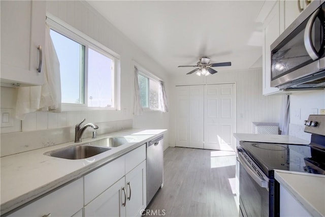 kitchen featuring sink, appliances with stainless steel finishes, light stone countertops, light hardwood / wood-style floors, and white cabinets