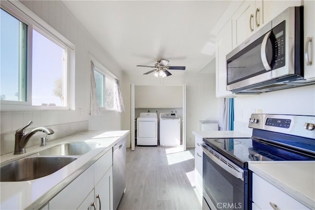 kitchen with sink, light wood-type flooring, independent washer and dryer, stainless steel appliances, and white cabinets