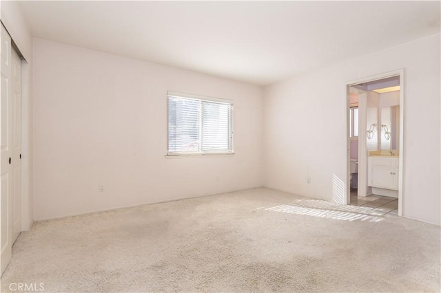 unfurnished bedroom with light colored carpet, ensuite bathroom, and a closet