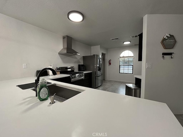 kitchen with wall chimney range hood, sink, a textured ceiling, and appliances with stainless steel finishes