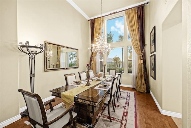 dining area with ornamental molding, wood-type flooring, a chandelier, and a towering ceiling