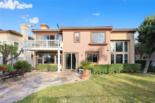 back of property with a balcony, a patio, and a lawn