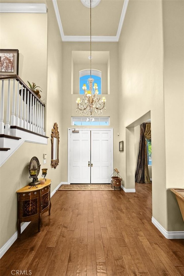 entrance foyer with crown molding, a towering ceiling, hardwood / wood-style floors, and a notable chandelier