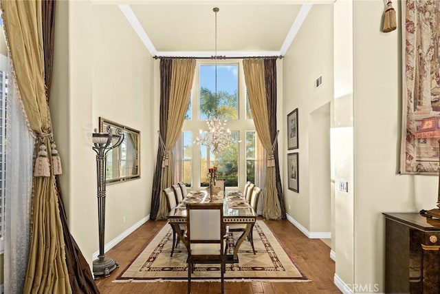 dining area with hardwood / wood-style flooring, ornamental molding, a high ceiling, and a chandelier